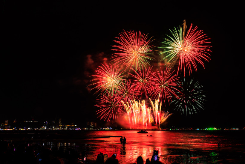 Thailand Pattaya Farbenfrohes Feuerwerk in Rot und Grün über dem Meer in Pattaya. Menschen stehen am Strand und beobachten das Lichtspektakel.