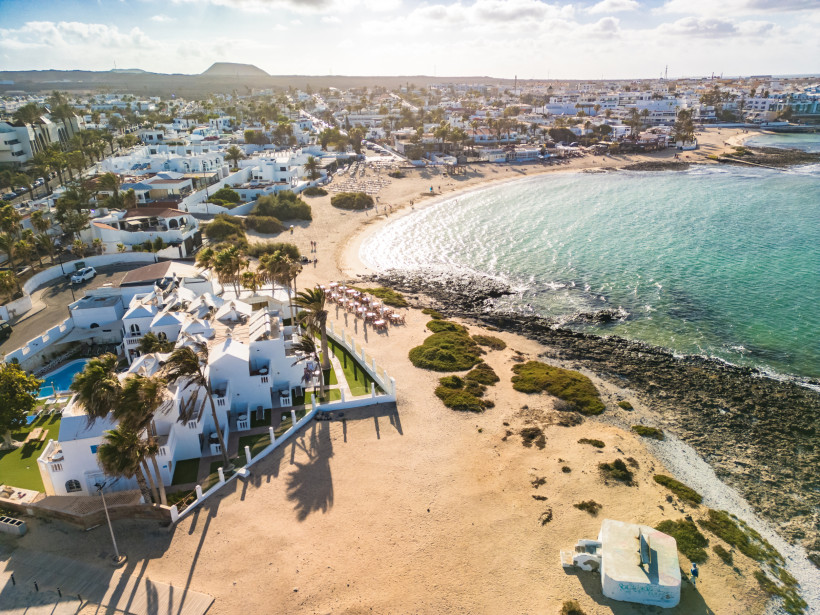 Luftaufnahme der Küstenbucht in Corralejo mit Sandstrand, Felsenriff und weißer Bebauung