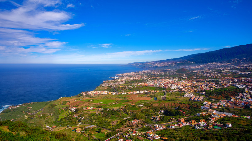 Panoramablick auf Teneriffas Nordküste bei La Orotava Panoramablick über die Nordküste Teneriffas mit der Stadt La Orotava und dem atlantischen Ozean. Im Vordergrund fruchtbare Felder, kleine Dörfer und grüne Hügellandschaft, im Hintergrund der blaue Ozean unter einem sonnigen Himmel mit leichten Wolken.