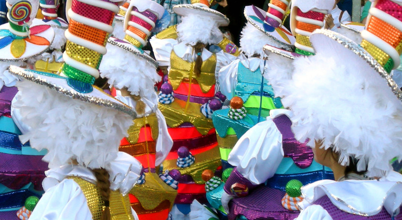 Fuerteventura Menschen in bunten, glitzernden Karnevalskostümen mit Cupcake-Design und hohen Zuckerstangen-Hüten. Die Kleidung ist mit Pailletten, Federn und leuchtenden Farben geschmückt.