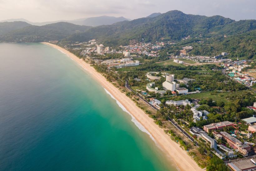 Luftaufnahme vom Karon Beach auf Phuket mit goldenem Sandstrand, türkisfarbenem Wasser und grünen Hügeln im Hintergrund – einer der schönsten Strände Thailands.