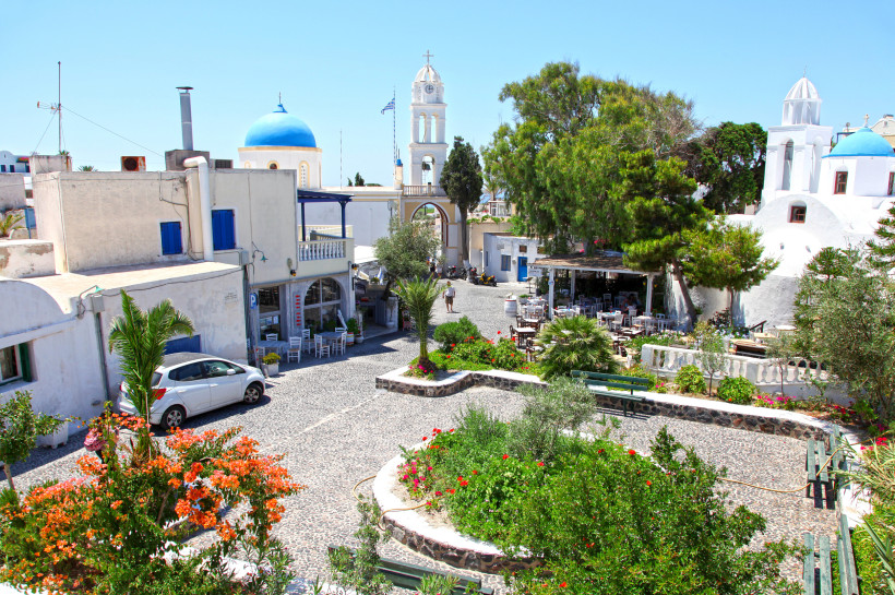 Santorini - Megalochori Megalochori auf Santorini: blumengeschmückter Dorfplatz mit weiß gekalkten Häusern, blauem Kuppeldach und Kirchturm-Bogen; Tavernen unter Bäumen