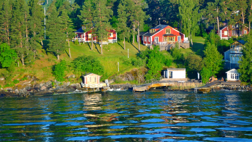Uferansicht in den Stockholmer Schären mit roten Holzhäusern und Bootsstegen Häuser am bewaldeten Ufer der Stockholmer Schären mit Stegen am Wasser