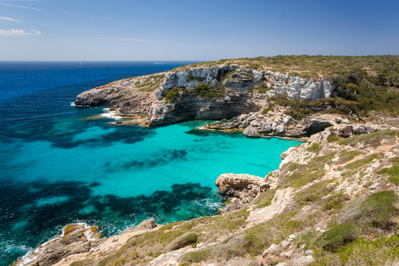 Mallorca - Cala Marmols Eine felsige Küstenlandschaft auf Mallorca mit atemberaubend türkisfarbenem Wasser, das sanft in die felsigen Buchten fließt. Die steilen Klippen sind mit mediterraner Vegetation bewachsen und rahmen die Bucht malerisch ein. Das Wasser zeigt unterschiedli