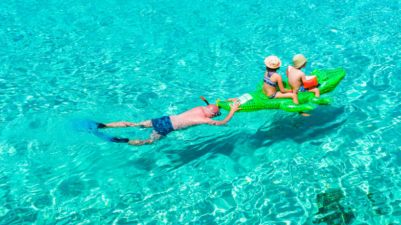 Kinder im ruhigen Meer beim Spielen auf aufblasbarem Schwimmtier, Familienurlaub