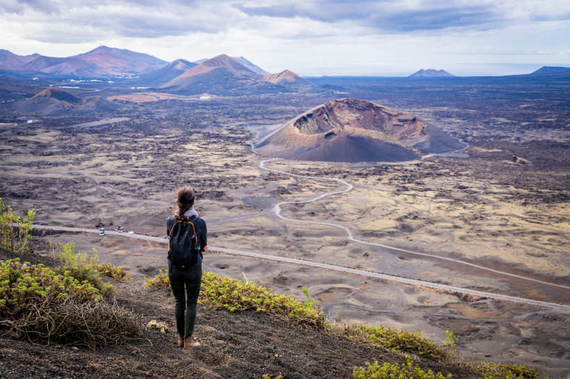 Frau wandert durch die vulkanische Landschaft des Timanfaya Nationalparks auf Lanzarote mit Blick auf Krater und Lavafelder