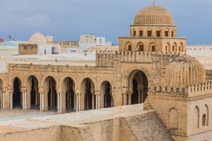 Die imposante Große Moschee von Kairouan in Tunesien. Das Foto zeigt die monumentale Architektur mit ihren massiven Torbögen, kunstvollen Kuppeln und detailreichen Mauern. Die Moschee thront majestätisch inmitten traditioneller Gebäude und strahlt eine be