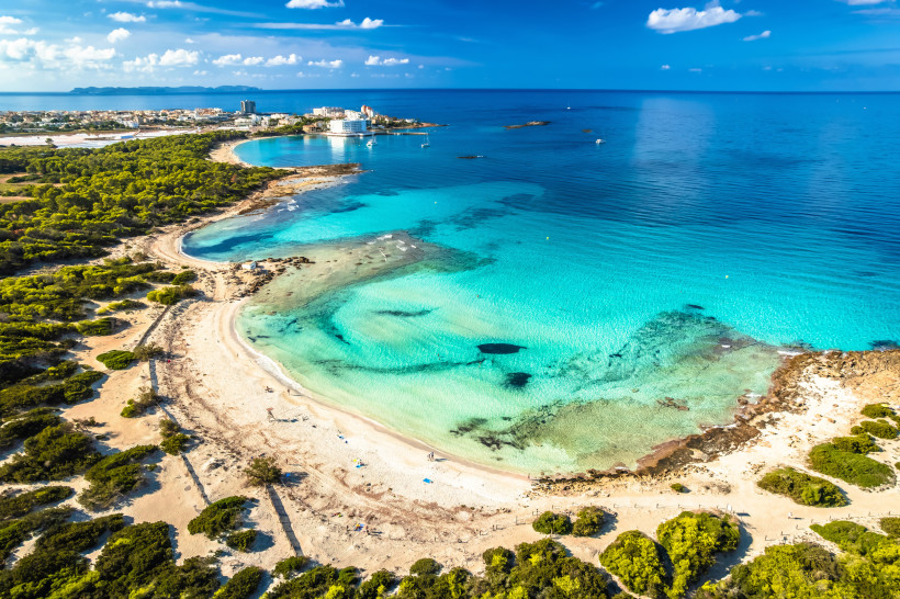 Luftaufnahme der Playa de es Trenc auf Mallorca mit hellem Sandstrand, flacher türkisfarbener Lagune und Pinienbewuchs