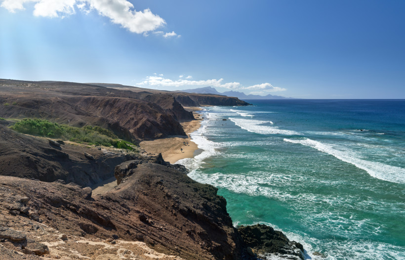 Steilküste mit Sandstrand Playa de la Pared auf Fuerteventura, türkisblaues Meer mit Wellen, im Hintergrund Berglandschaft