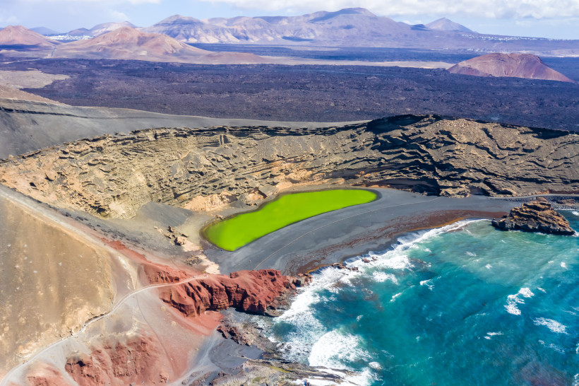 Atemberaubende Aussicht auf den Charco de los Clicos – grüner Kratersee in einzigartiger Vulkanlandschaft Luftaufnahme des Charco de los Clicos in El Golfo auf Lanzarote mit grünem Kratersee, schwarzem Strand und vulkanischer Küstenlandschaft.