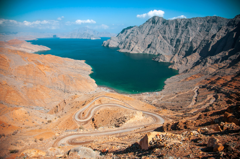 Blick über die Musandam-Fjorde mit türkisblauem Wasser, felsigen Bergen und Serpentinenstraße im Vordergrund