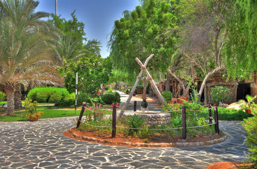 Traditionelles Heritage Village in Abu Dhabi mit Palmen, grünen Bäumen, Steingartenwegen und dekorativem Brunnen inmitten einer parkähnlichen Anlage