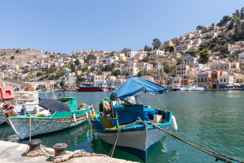 Kleiner Hafen auf Rhodos mit bunten Häusern am Hang, traditionellen Fischerbooten und ruhigem Wasser
