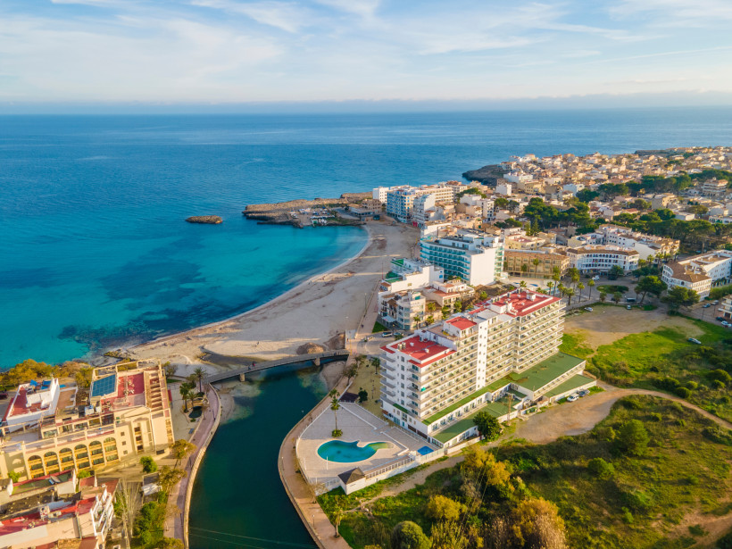 Luftaufnahme der Bucht Cala Moreia mit Sandstrand, türkisfarbenem Meer und Hotels an der Küste