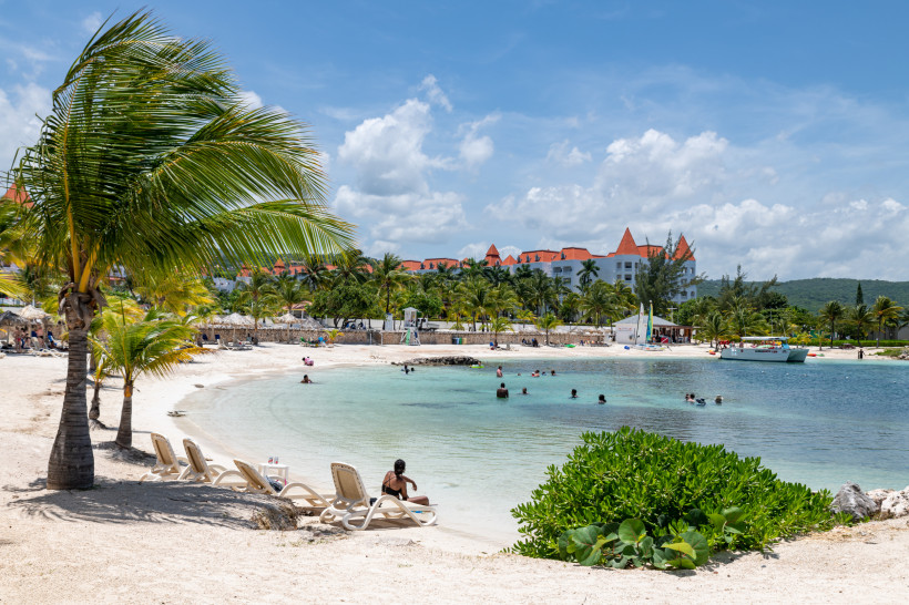 Karibikstrand mit Palmen und Sonnenliegen – entspannter Badeurlaub unter der Sonne Karibischer Strand mit Sonnenliegen, Palmen und türkisfarbenem Wasser – Urlauber genießen das tropische Klima vor einer Resortanlage.