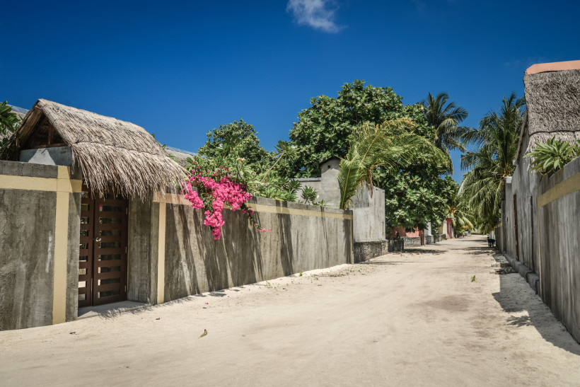Leere sandige Straße in einem traditionellen maledivischen Dorf mit Palmen und niedrigen Mauern
