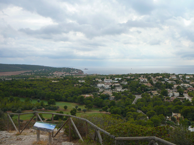 Blick vom Puig de sa Morisca über Wald- und Siedlungsgebiet zur Küste und zum Meer unter bewölktem Himmel