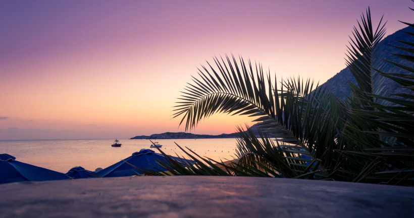Sonnenaufgang am Strand von Bali auf Kreta mit Palmenblatt im Vordergrund und Booten auf dem Meer