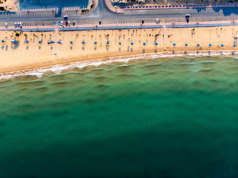 Luftaufnahme des Flamingo Beach in Ras Al Khaimah mit Sonnenschirmen und türkisfarbenem Meer.