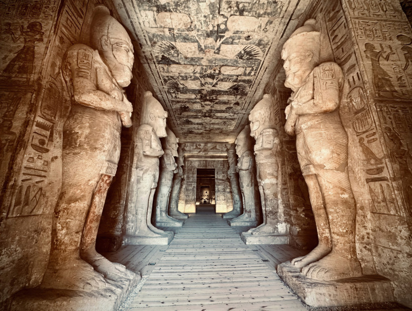 Das Bild zeigt den beeindruckenden Säulengang im Inneren des Tempels von Abu Simbel. Beidseitig des Ganges stehen monumentale Statuen des Pharaos Ramses II. in der Gestalt des Gottes Osiris. Die Wände und Decken sind mit gut erhaltenen Hieroglyphen und Re