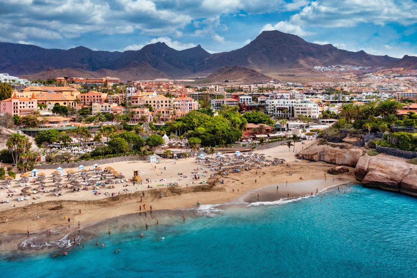 Playa del Duque: Strandabschnitt mit türkisfarbenem Meer, Hotels und Bergen im Hintergrund Playa del Duque mit Sandstrand, Badegästen und Promenade vor Bergkulisse
