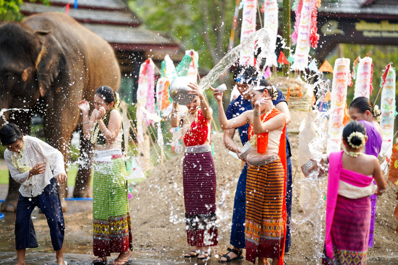 Thailand - Koh Samui Das Bild zeigt eine lebhafte Szene des thailändischen Wasserfestes Songkran. Männer, Frauen und Kinder in farbenfroher, traditioneller Kleidung lachen und spritzen sich gegenseitig mit Wasser aus Schalen und Gefäßen. Wasser fliegt durch die Luft und sorgt