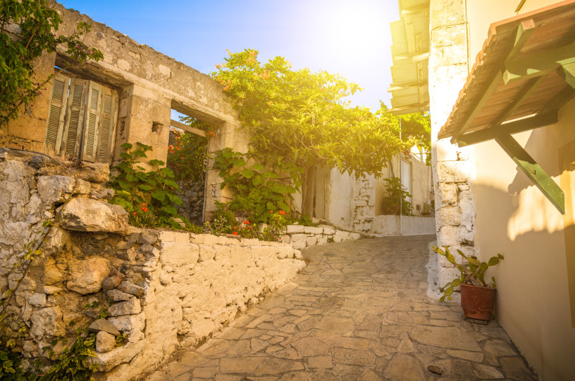 Schmale gepflasterte Gasse mit alten Steinhäusern und üppiger Vegetation im Old Village Malia