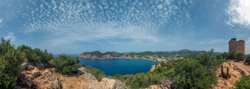 Blick von der Torre de Cap Andritxol über eine Bucht mit Küstenlinie, Meer und Hügeln unter wolkigem Himmel