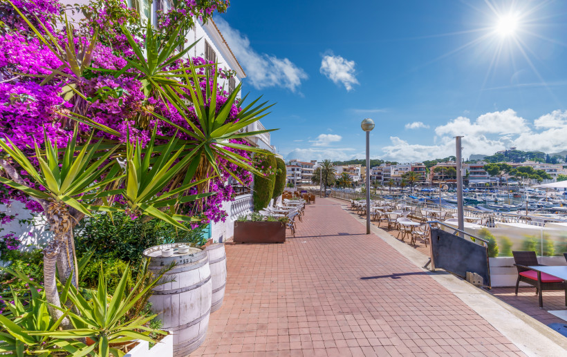 Promenade von Cala Ratjada mit Blumen, Palmen, Restaurants und Blick auf den Hafen auf Mallorca