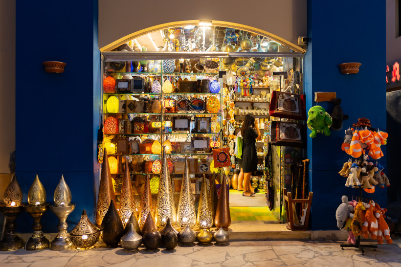 Ägypten - Marsa Alam Souvenirshop mit orientalischen Lampen, Keramik, Taschen und Plüschtieren. Eine Frau schaut sich im Laden um. Die Szenerie ist farbenfroh und abends beleuchtet.