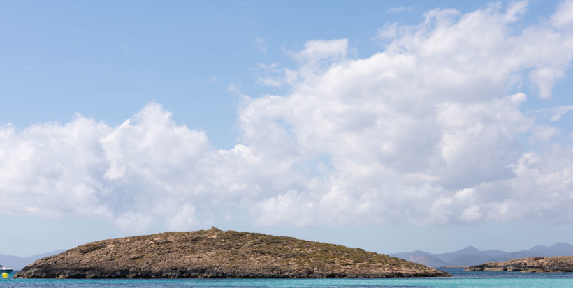 Illa des Conills, felsige Insel im Meer unter wolkigem Himmel Niedrige, felsige Insel Illa des Conills vor blauem Meer und wolkigem Himmel