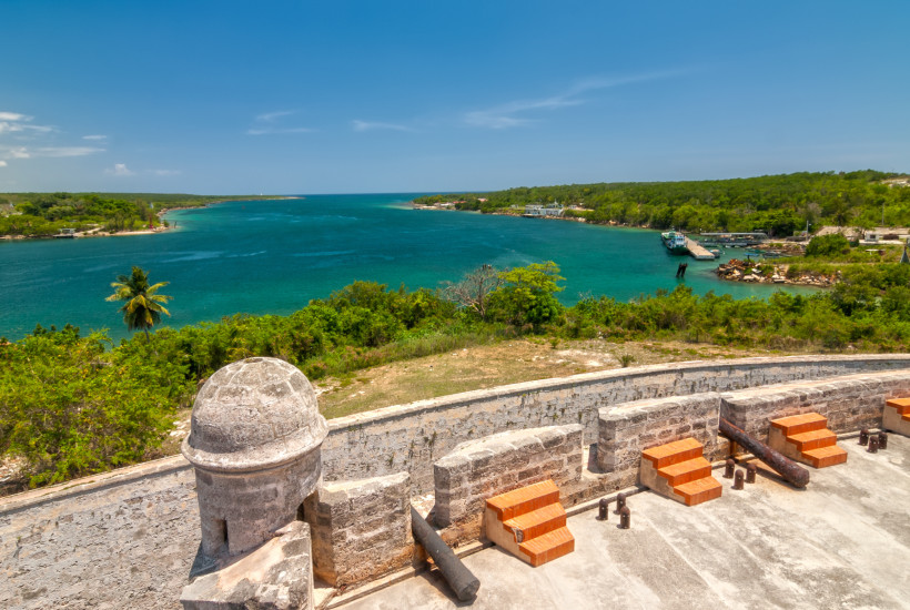 Blick von der historischen Festung Castillo de Jagua auf die Bucht von Cienfuegos auf Kuba mit türkisblauem Wasser, üppiger Vegetation und Hafenanlage im Hintergrund.