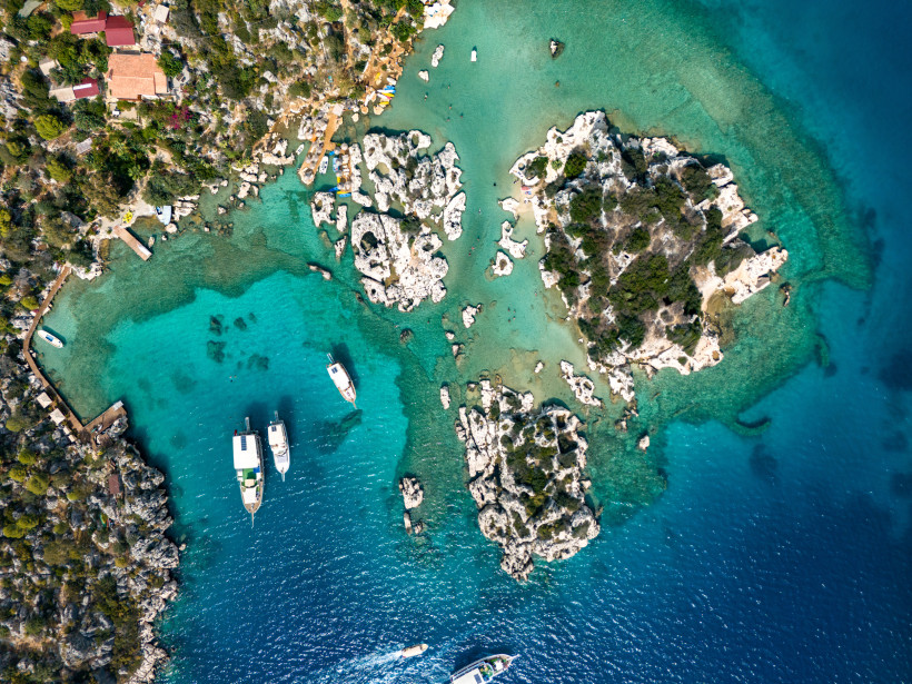 Eine traumhafte Luftaufnahme zeigt kristallklares Wasser, kleine Inseln und Boote vor der felsigen Mittelmeerküste 