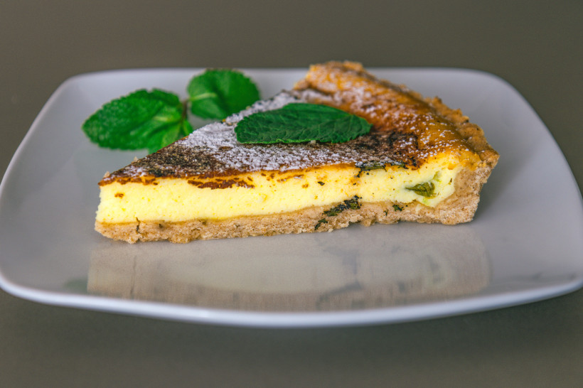 Quiche-Stück auf weißem Teller mit Kräuterfüllung und Minzblättern Stück Quiche mit Kräutern auf weißem Teller, mit Minzblättern garniert
