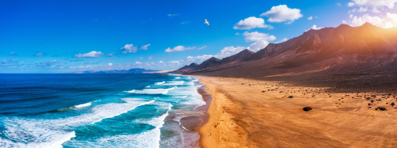 Playa de Cofete – Spektakuläre Drohnenaufnahme des wilden Naturstrands auf Fuerteventura Luftaufnahme der beeindruckenden Playa de Cofete auf Fuerteventura mit türkisblauem Meer, weiten Sandflächen und der Bergkette im Hintergrund.