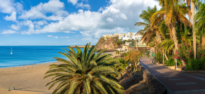 Sonnige Promenade von Morro Jable mit Palmen, Meerblick und hellem Sandstrand auf Fuerteventura.