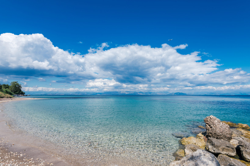Strand Agios Ioannis Peristeron, Korfu Küstenansicht am Strand Agios Ioannis Peristeron auf Korfu mit klarem Wasser, Kiesufer und Wolkenhimmel