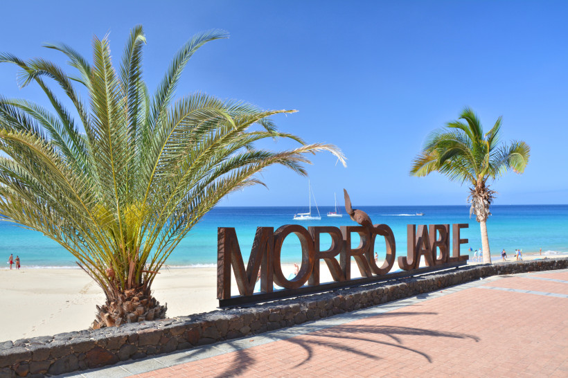 Strandpromenade in Morro Jable mit Palmen, Meerblick und großem Schriftzug 