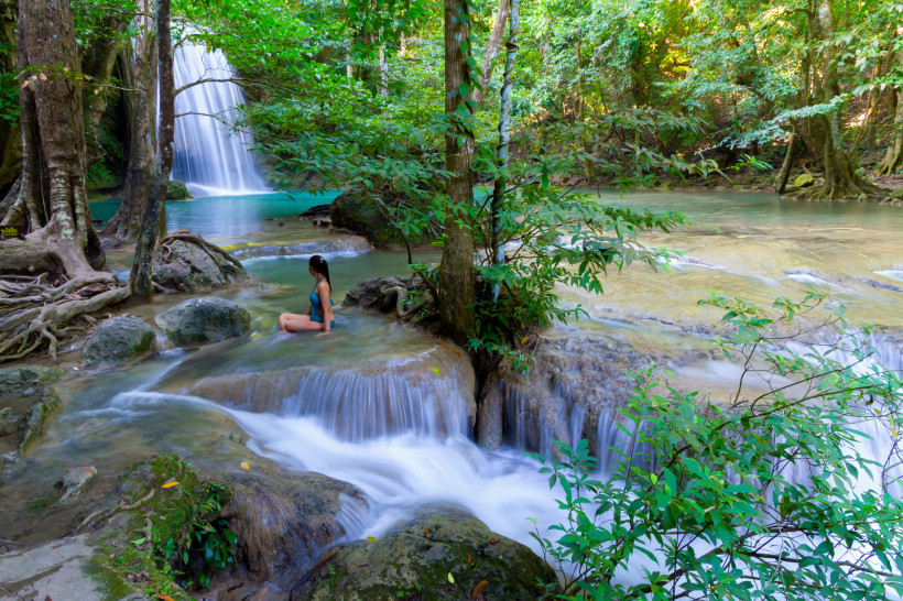 Erawan Wasserfälle Thailand – Tropische Natur Frau sitzt am Naturbecken der Erawan-Wasserfälle im Erawan Nationalpark in Thailand, umgeben von tropischem Dschungel und türkisblauem Wasser.