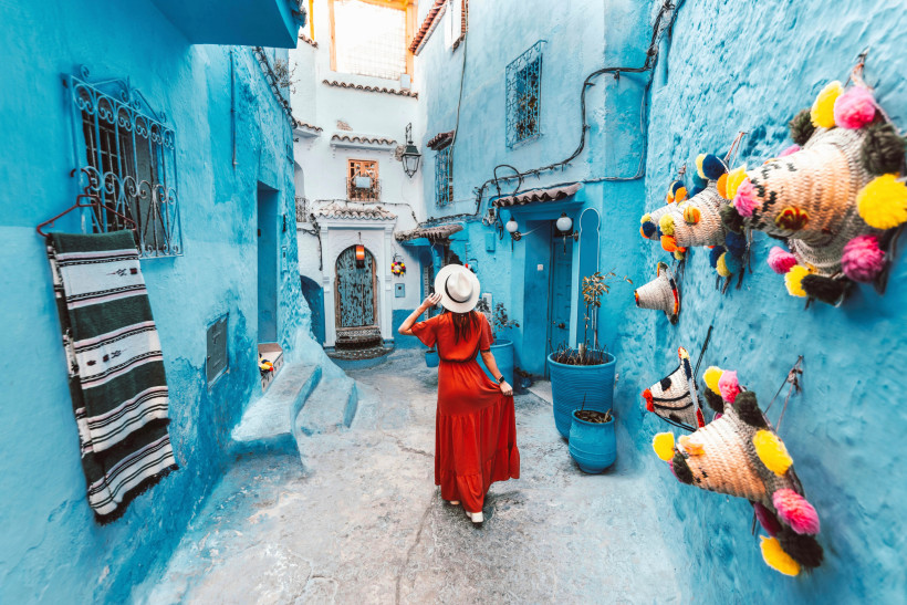 Blaue Altstadtgasse in Chefchaouen – Marokkos Fotomotiv Frau in rotem Kleid spaziert durch eine enge, blau gestrichene Gasse in der Altstadt von Chefchaouen, Marokko – beliebtes Fotomotiv und Sehenswürdigkeit.