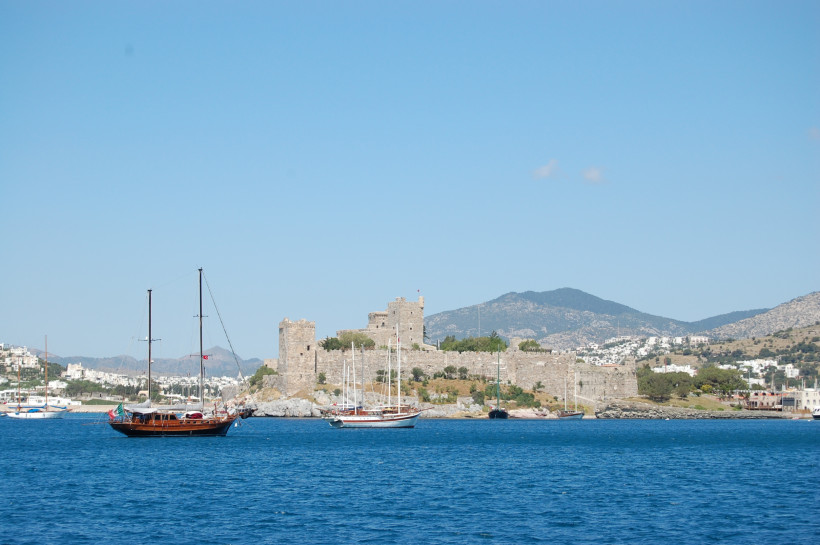 Blick über das Meer auf die Burg von Bodrum mit Segelbooten im Hafen und der Küstenstadt im Hintergrund
