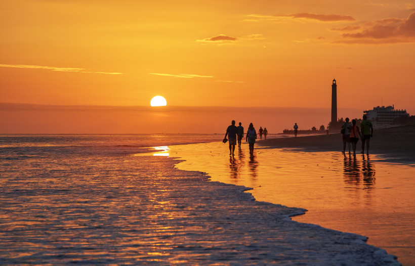 Sonnenuntergang am Strand von Playa del Inglés mit Menschen am Ufer und Leuchtturm im Hintergrund