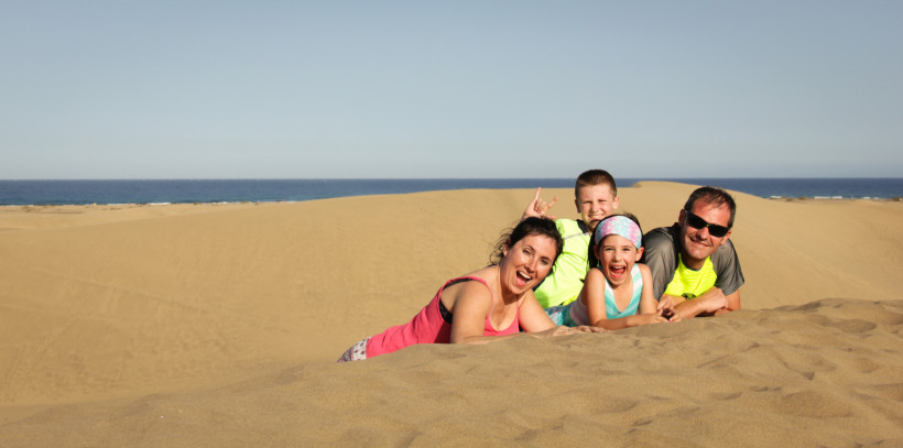 Gruppe liegt in den Sanddünen von Maspalomas, im Hintergrund das Meer