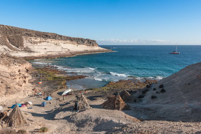 Küstenbucht bei Adeje auf Teneriffa mit hellem Fels, kleiner Strandfläche und Segelboot vor der Küste