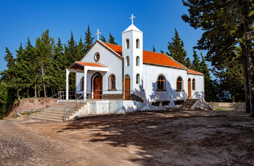 Kleine weiß getünchte Kapelle mit rotem Ziegeldach und Glockenturm, gelegen an einem Waldweg. Die Kirche ist von Bäumen umgeben und strahlt in der Nachmittagssonne