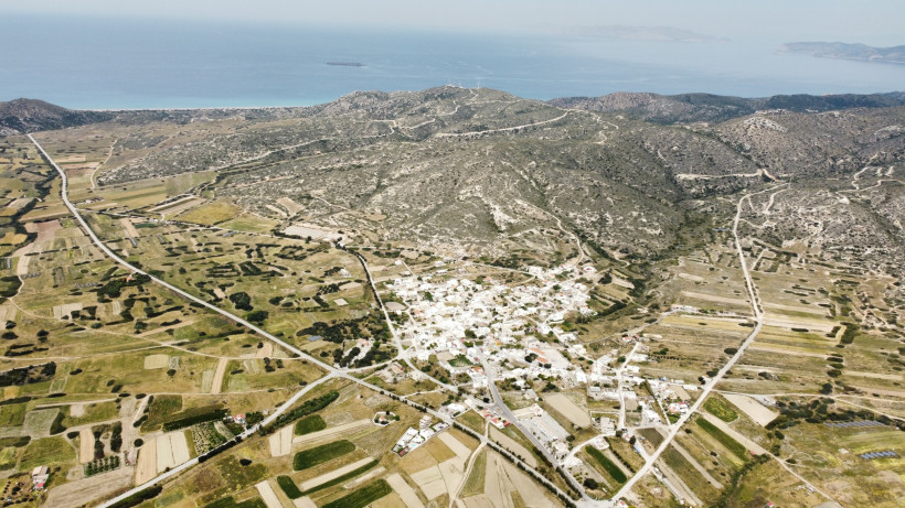 Drohnenaufnahme eines Dorfes auf Rhodos, umgeben von Feldern, Hügeln und weiter Landschaft mit Meerblick