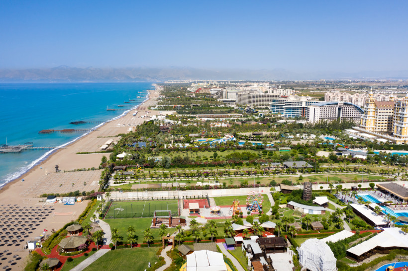 Lara Beach an der Türkischen Riviera – Luxusresorts, Strandpromenade und kristallklares Meer Luftaufnahme von Lara Beach an der Türkischen Riviera mit breitem Sandstrand, langen Hotelstegen, luxuriösen Resorts und Blick auf die Küstenlandschaft.