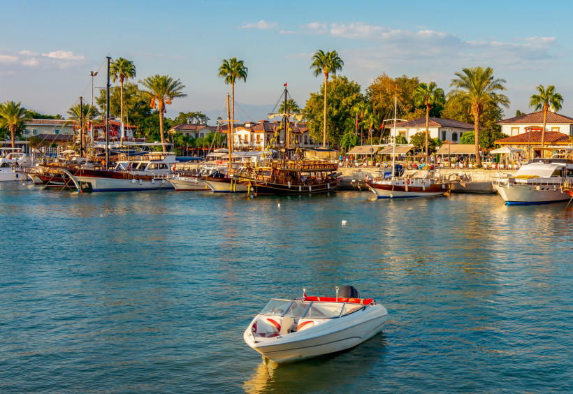 Hafen von Side mit Ausflugsbooten, Palmen und Cafés direkt am Wasser bei sonnigem Wetter