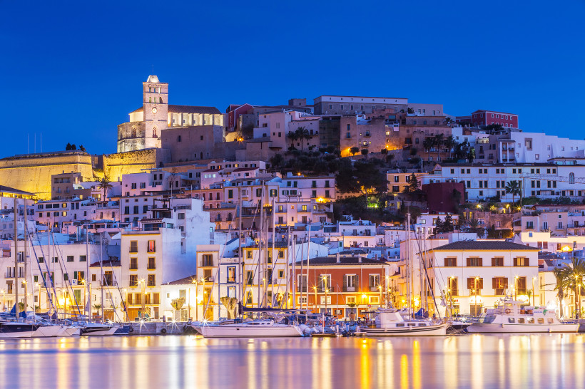Dalt Vila in Ibiza-Stadt am Abend mit beleuchtetem Hafen und Segelbooten