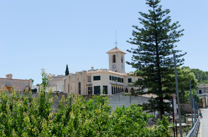 Kirche mit Uhrturm und Kreuz in Escapdella, umgeben von Bäumen